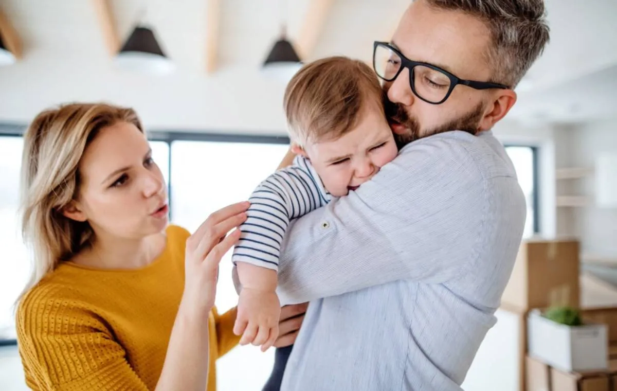 A young family with a crying toddler girl standing indoors at home